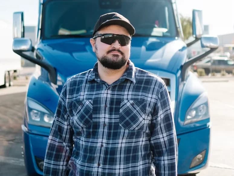A driver standing in front of a blue semi truck